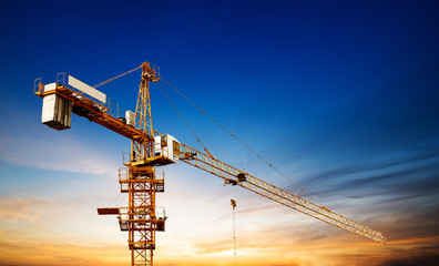 Industrial construction cranes and building silhouettes over sun at sunrise.