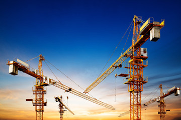 Industrial construction cranes and building silhouettes over sun at sunrise.