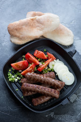 Grill pan with roasted balkan cevapcici sausages served with tomatoes, onion and pitas