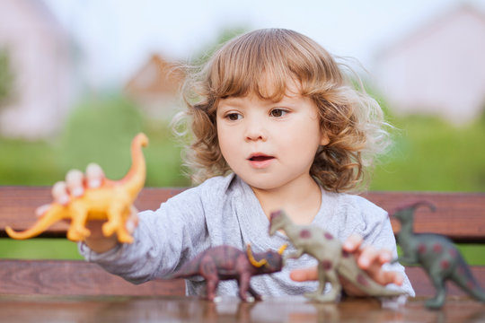 Toddler kid playing with a toy dinosaurs outdoors.