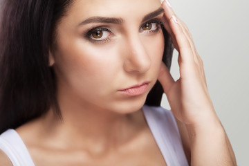 A tired, exhausted young woman who suffers from a severe headache of tension. Sufferers from headache. Migraines A sense of pressure and stress. On a gray background.