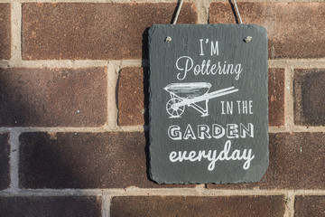 I’m pottering in the garden everyday slate garden sign hanging against a brick wall
