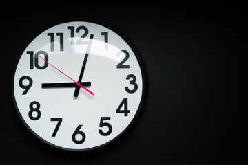 Realistic classic dark and white round wall clock, isolated on black background. selective focus.