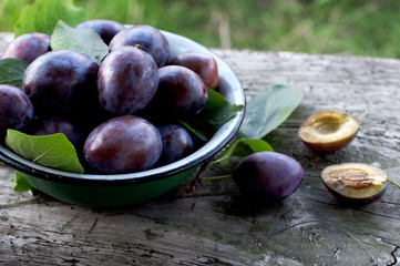 Ripe plums in plate on wooden background