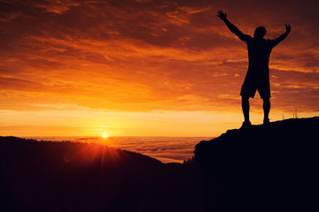 Man silhouette on the mountain top watching the sunset over clouds and forest