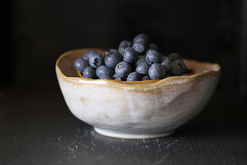 Blueberry .  blueberries in a light gray clay cup on a black background. Dark Key. The harvest of blueberries