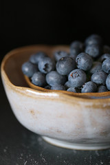 Blueberry . ripe blueberries in a light gray clay cup on a black background. Dark Key. The harvest of blueberries