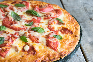 Hot Homemade Pepperoni Pizza on a rustic wooden table. Pizza with tomato, cheese and basil with copy space