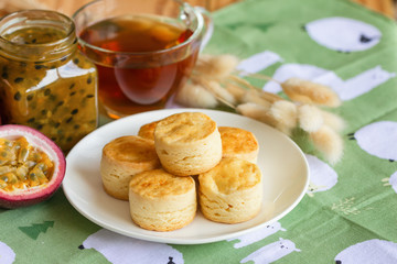 Homemade plain scones serve with homemade passion fruit jam. Scones is traditional English pastry for afternoon tea or coffee break. Delicious plain scones ready to served on wood table.