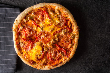 Cut into slices delicious fresh pizza with  pepperoni on a dark background. Top view . Pizza on the black table.
