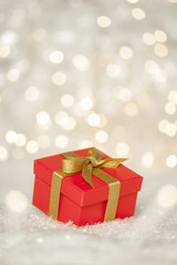 Red Holiday Christmas Present Gift on snow with sparkling Bokeh lights in the Background