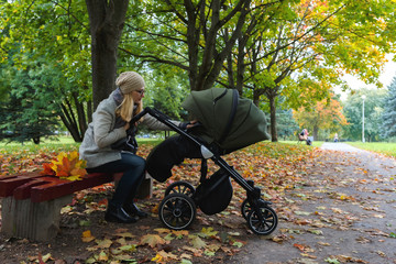 A young girl in a coat with a hat with a baby stroller and a child wearing a hat and rests on a...