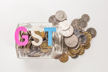 The word GST (Goods and services tax) with coins spill over glass bottle isolated white  background