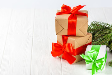 Obraz na płótnie Canvas Craft gift boxes with red, green ribbon and bow, green Christmas tree, decorations, on white wooden background.
