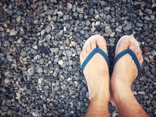 Feet of a man wearing sandals or flip flops on the old stone concrete floor for summer time vacation attribute, slippers, shoes. Summer holiday and vacation concept vintage tone with copy space.