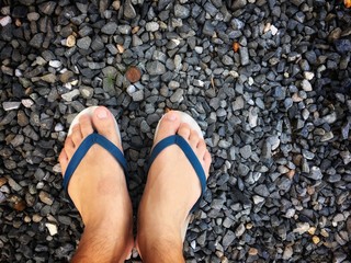 Feet of a man wearing sandals or flip flops on the old stone concrete floor for summer time vacation attribute, slippers, shoes. Summer holiday and vacation concept vintage tone with copy space.