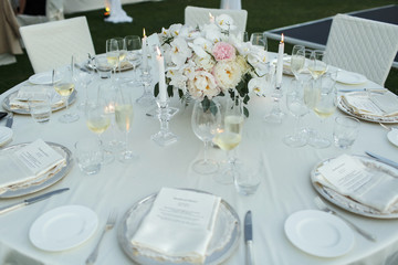 White chairs stand around white table prepared for wedding dinner