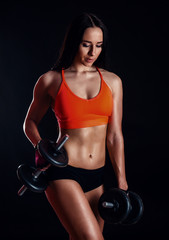 Nice sexy girl doing workout with dumbbells isolated over black background. Athletic young woman do a fitness workout with weights.