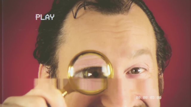 Fake VHS tape: a funny ugly man looking at the camera with a magnifying lens (parody of a spy), searching for valued information.
