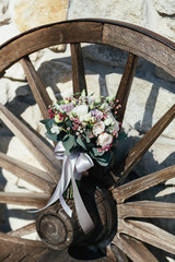 Rich wedding bouquet of white and violet roses lies on wooden wheel