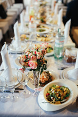 Little glass vase with pink roses stands on a dinner table