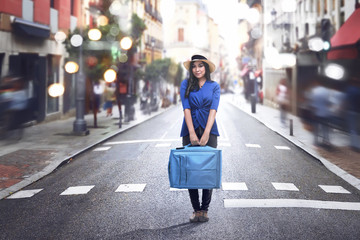 Smiling asian woman wearing hat and holding suitcase