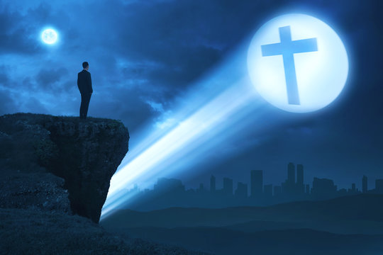 Man looking bright cross on the edge of cliff