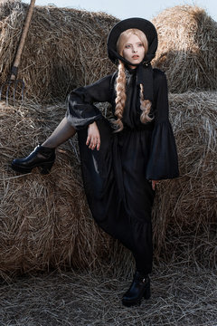 Fashion young woman wearing stylish black dress and hat at countryside. Amish fashion style.