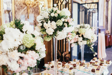 Tall vases with roses stand on layered dinner table with chocolate cakes and cookies
