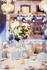 Tall vase with white and green flowers stands on round dinner table number eight