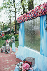 Wedding altar made of blue cloth, pink flowers and waterfall stands in a green forest
