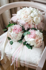 Three wedding bouquets mae of white and pink flowers with ribbons and feather lie on the chair