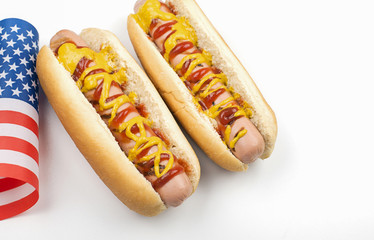 Two hotdogs with ketchup and mustard next to American flag on white background. Isolated. Fastfood.