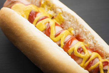 Close-up of hotdog with ketchup and mustard on black background. Fastfood.