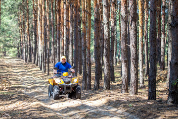 Caucasian man inyellow cap riding an ATV quad bike over rough terrain in pine autumn forest. Adventure activity concept