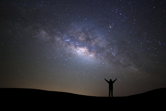 Landscape with milky way galaxy, Starry night sky with stars and silhouette of a standing sporty man with raised up arms on high mountain.