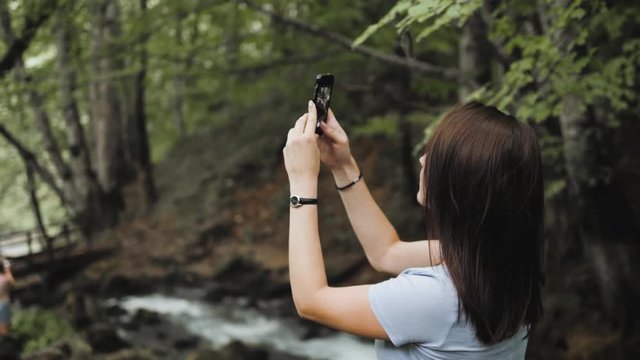 Tourist Girl Taking Photo By Phone, Small Waterfall Flowing Down The Rocks, Mountain River Raging Among The Rocks In The Forest, Caucasian mountains, Europe.