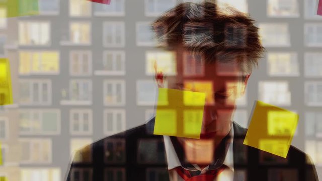 Reflection of a businessman putting post it notes on to a window at night with a modern apartment block behind.