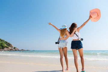 Portrait of two young asian female friends walking on the sea shore turn back at camera laughing. Multiracial young women strolling along a beach. - Powered by Adobe