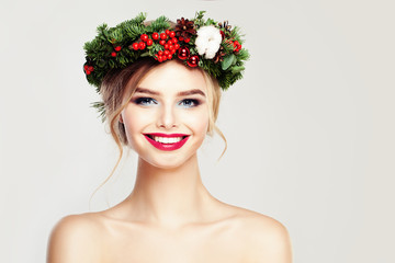 Beautiful Smiling Woman Fashion Model. Happy Girl with Christmas or New Year Wreath with Green Xmas Tree Twig, Red Decor and Berry. Cute Female Face Closeup