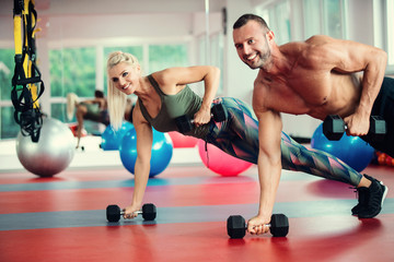 Fototapeta premium Young couple working out with dumbbells at gym