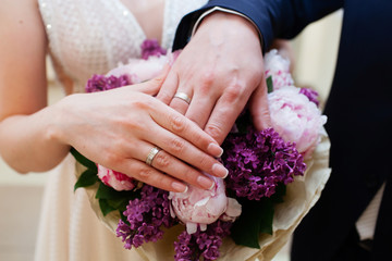 Bride and groom hands with wedding rings and bridal bouquet