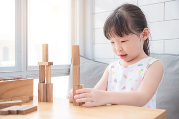 Naklejka premium Little asian girl playing wooden blocks on table in living room