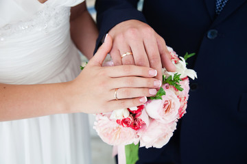 Bride and groom hands with wedding rings and bridal bouquet