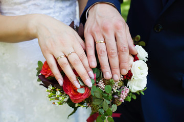 Bride and groom hands with wedding rings and bridal bouquet