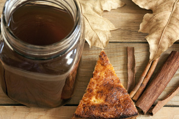 Autumn still-life of a hot drink, dry maple leaves, cinnamon and slice of warm homemade pie.
