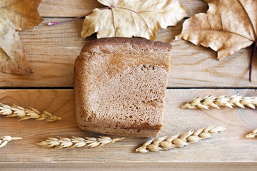 Half of the bread on the wooden table next to the wheat ears and dry autumn leaves