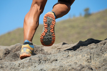 Athlete trail running in the mountains on rocky terrain, sports shoes detail 