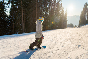 Female snowboarder riding the slope at winter ski resort in the beautiful evening, enjoying sunset