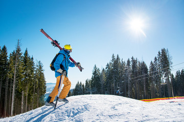 Shot of a male skier walking up the slope in the mountains carrying his gear on his shoulder on a...
